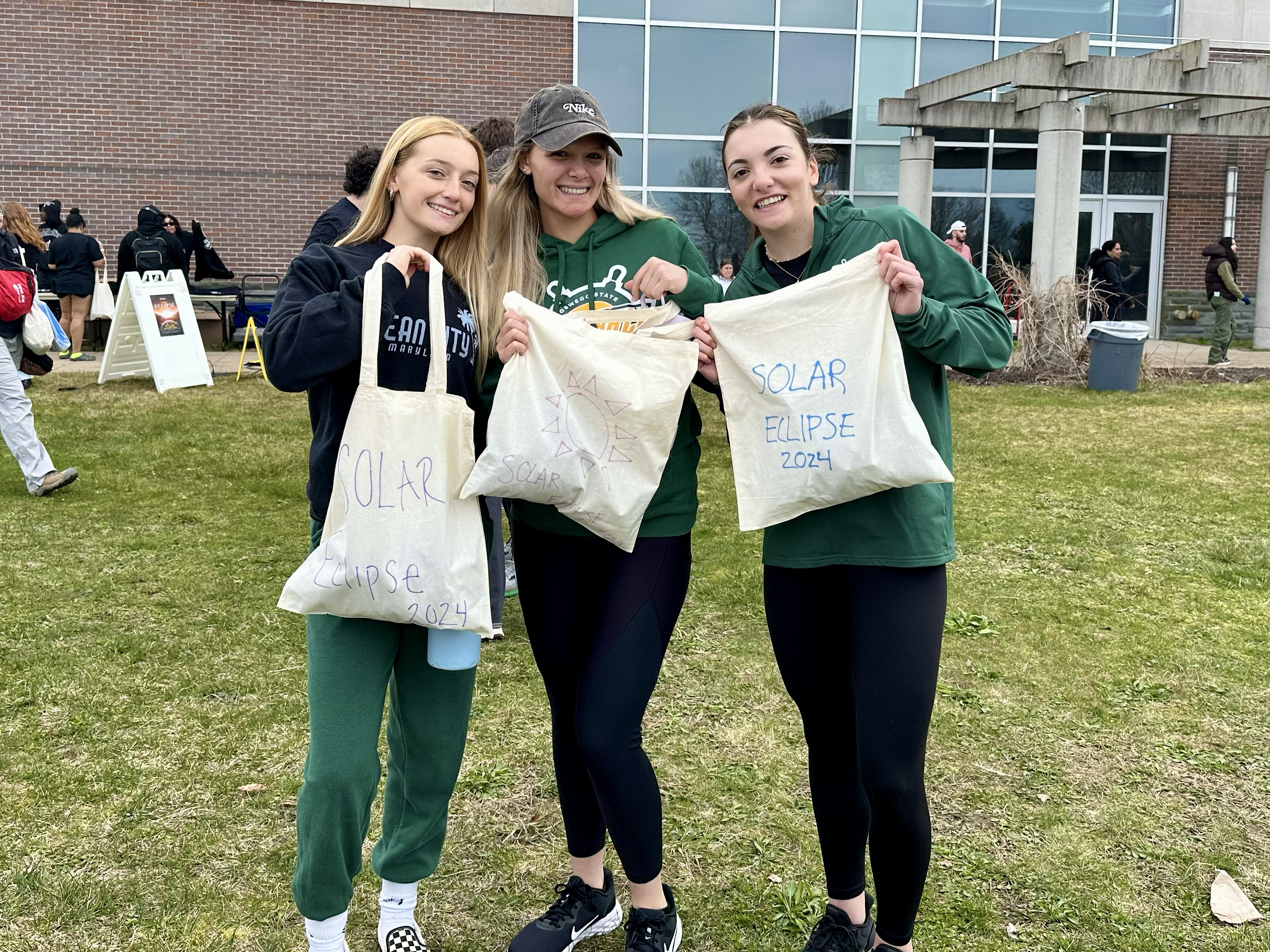 Students show off their eclipse-themed tote bags they created at the Solar Eclipse Watch Party held north of Marano Campus Center on Swetman Field.