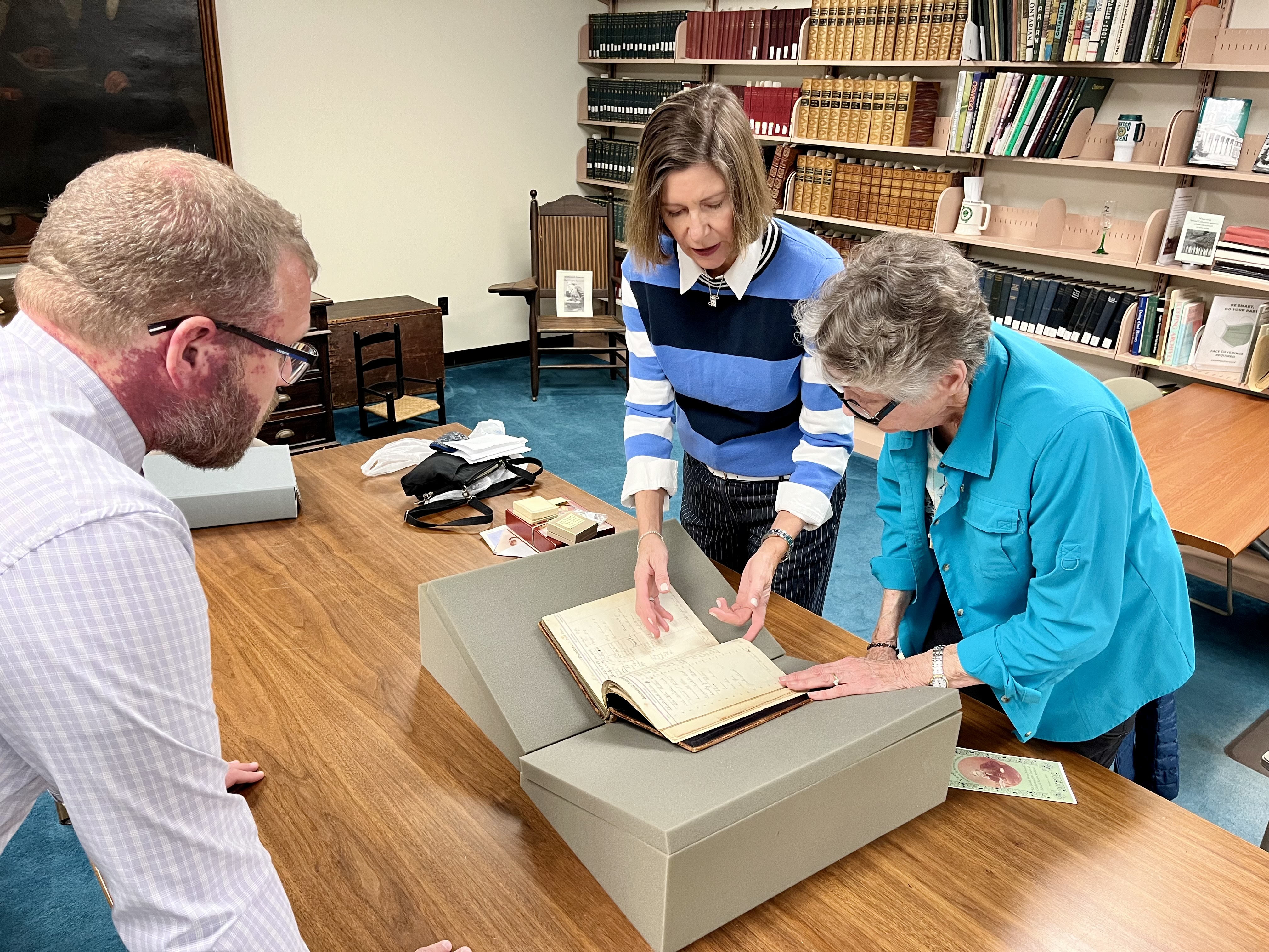 Two descendants of Edward Austin Sheldon – who founded the institution now known as SUNY Oswego – visited campus last week for research and conversations. Marianna Page (right), Sheldon’s great-great granddaughter, and her daughter Dawne Pafford (center) traveled from Illinois and Wisconsin, respectively. Here Zachary Vickery, university archivist librarian, shows them a recently discovered ancestral registry and Sheldon family ledger in Penfield Library’s Archives and Special Collections.