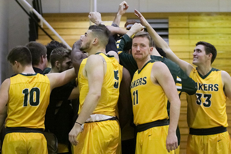 Men's basketball team huddles with their arms extended into the circle