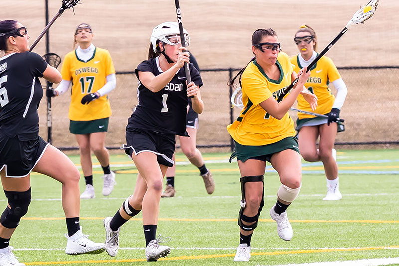 Women's lacrosse player Teresa Shattuck of Oswego runs past Potsdam defenders as she cradles the ball