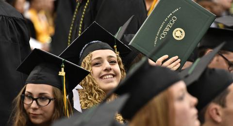 Student holds up her diploma booklet toward loved ones in audience