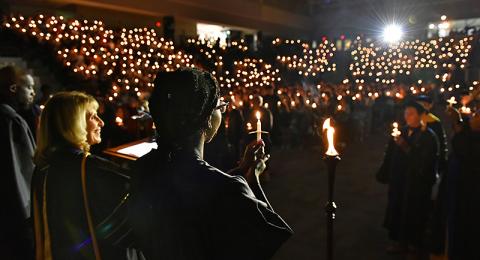 Platform party holds candles aloft, as does the audience, during the Welcoming Torchlight Ceremony