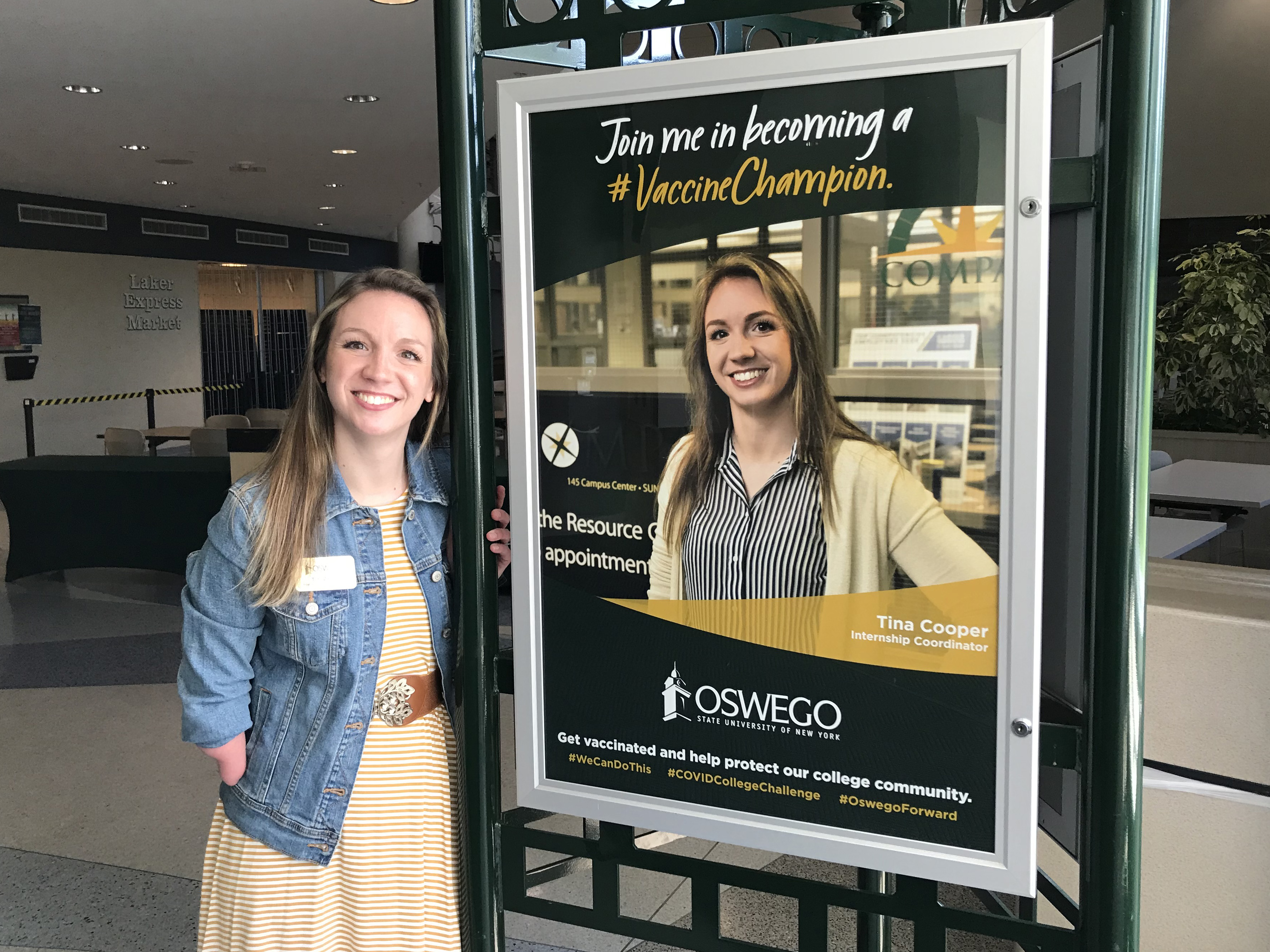 Tina Cooper, the college’s internship coordinator, poses next to a poster of her promoting SUNY Oswego joining the College Vaccine Champion Challenge, a national effort to increase vaccination rates for the benefit of public health