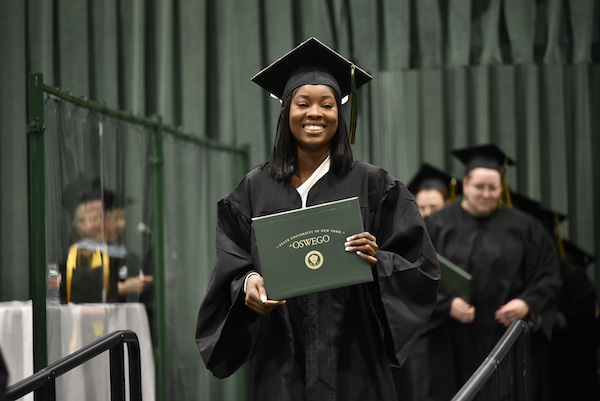 A student at Commencement, dressed in a cap and gown and holding her diploma