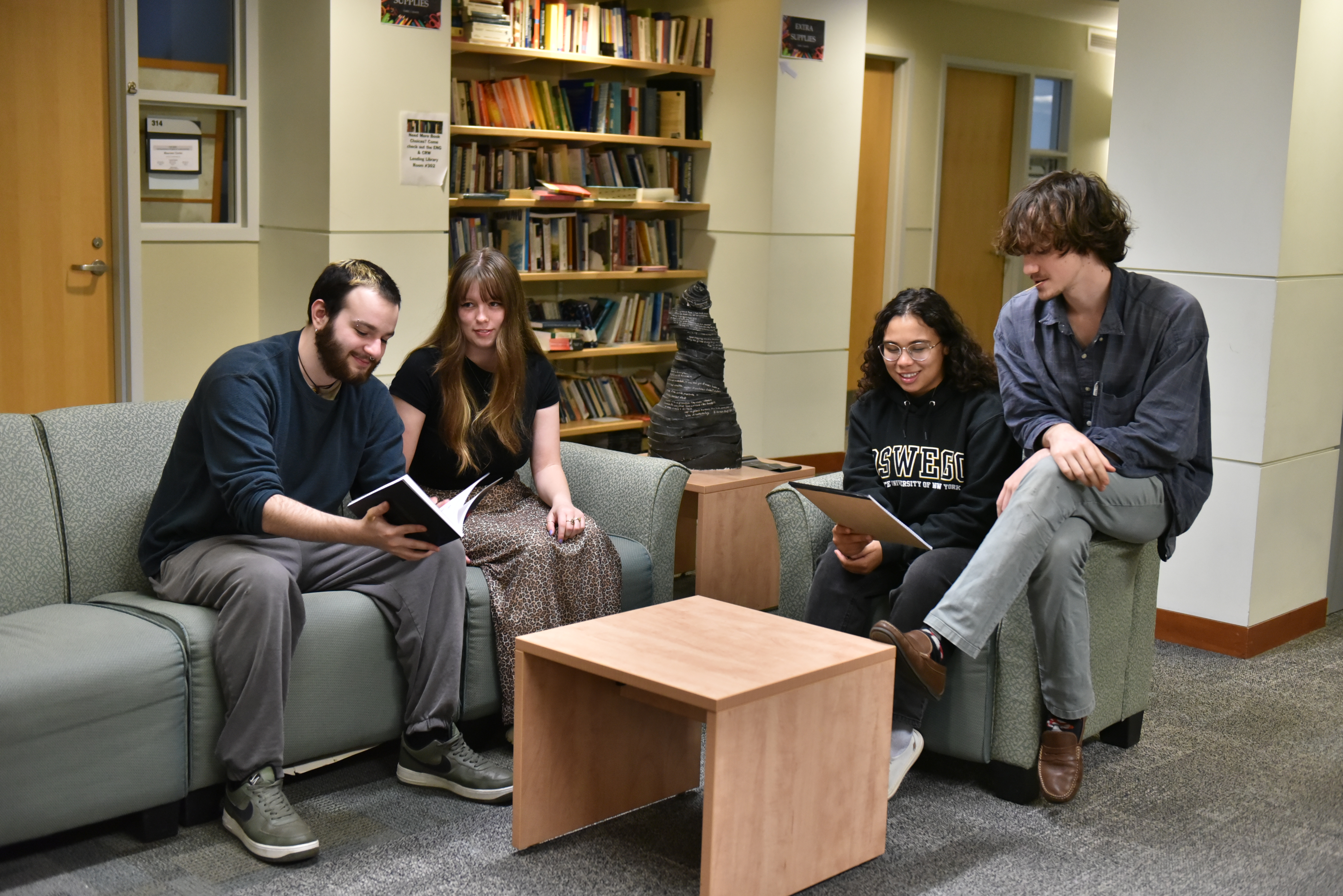 Four students sitting on couches in a lounge, with bookshelves behind them