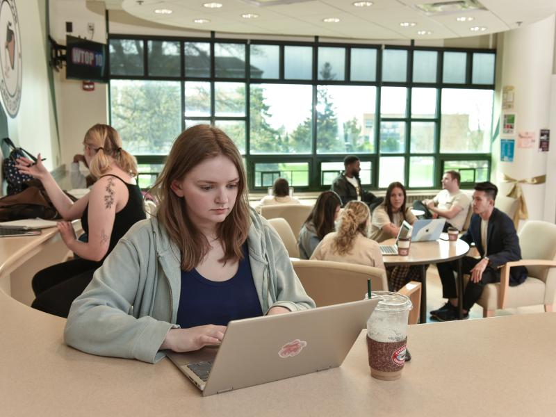 student working on a laptop with other people in the background