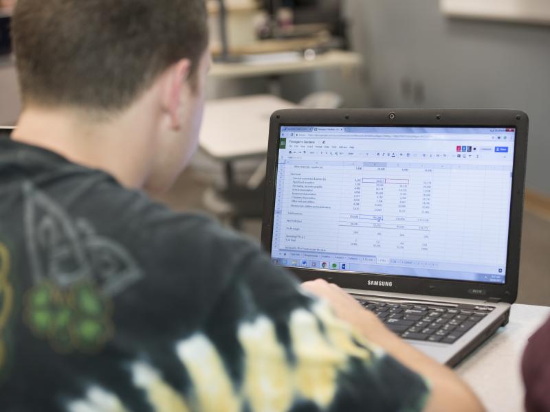 male student typing on a laptop with an excel file open