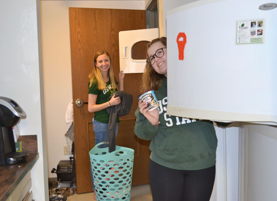 student takes and item out of her full size fridge while her roommate does her laundry in the kitchen of their village townhouse