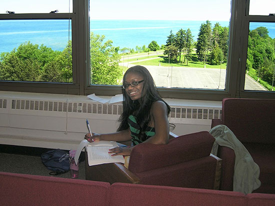 Female student studies in a Seneca Hall lounge looking over the lake on a beautiful summer day.