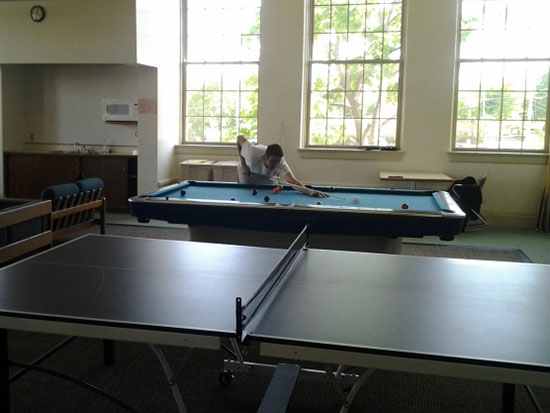 Student playing pool in Sheldon Hall main lounge. Kitchenette and ping-pong table too.