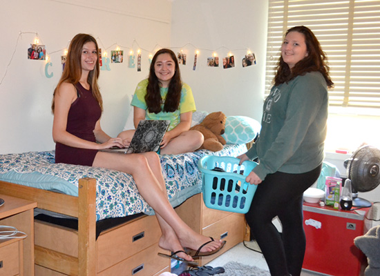 Students sit on their bed to study and chat with a friend on her way to the laundry room.