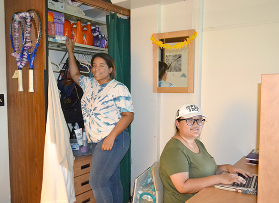Seneca hall resident reaches up to grab something from her floor-to-ceiling closet while her roommate works at her desk.