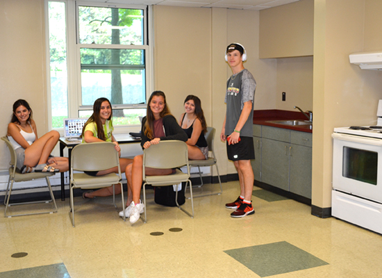 A group of residents study at a table in the kitchen area while doing their laundry next door in the Seneca Hall laundry room.