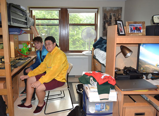 Male students in Johnson Hall work together in their room. The bed is bunked above a large worksurface with a hutch.
