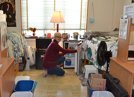 Student in her Funnelle Hall room taking milk out of her mini-fridge.