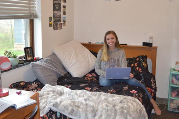 resident of the village townhouse sits on her full size bed in her fully furnished bedroom