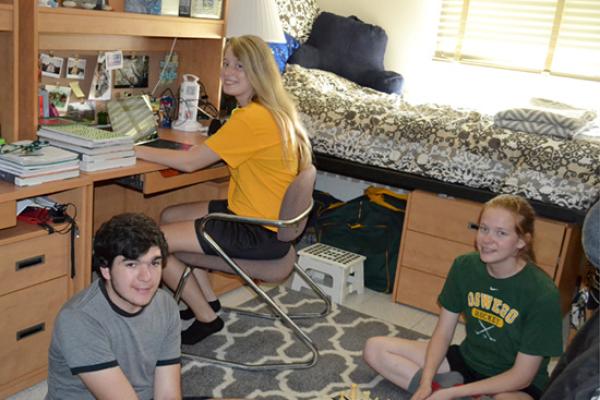 2 Oneida Hall residents do homework and play chess in their room with a friend.