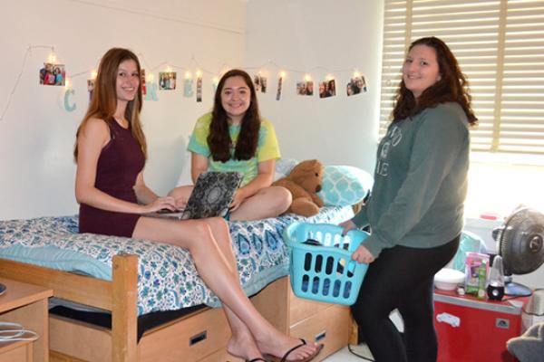 Students sit on their bed to study and chat with a friend on her way to the laundry room.