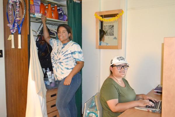 Seneca hall resident reaches up to grab something from her floor-to-ceiling closet while her roommate works at her desk.