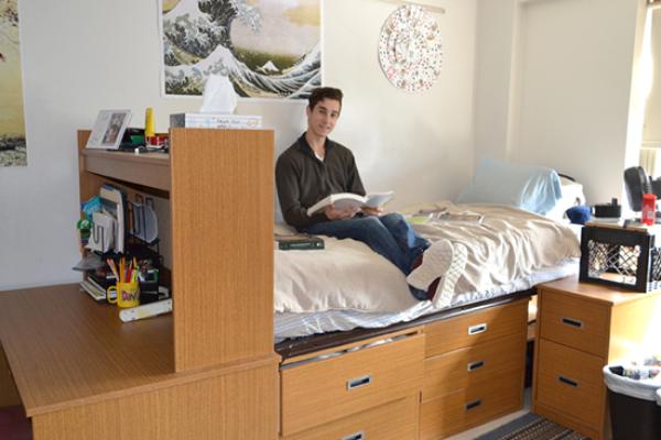 Hart Hall resident studies on his bed that is lofted high enough so that his dressers are slid underneath.