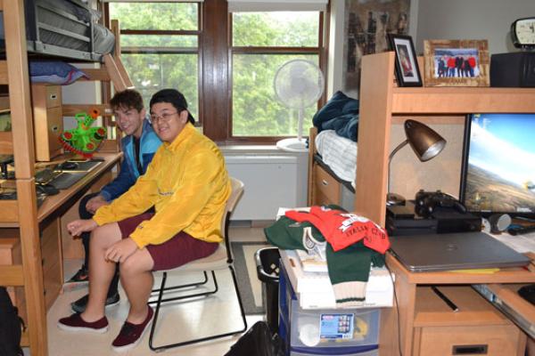 Male students in Johnson Hall work together in their room. The bed is bunked above a large worksurface with a hutch.