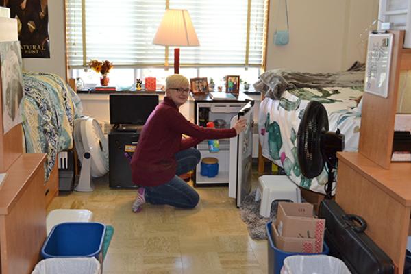 Student in her Funnelle Hall room taking milk out of her mini-fridge.