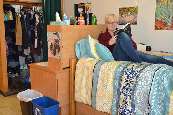 Student in her Funnelle Hall room reading and relaxing on her bed.