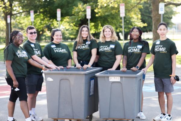 Seven Laker Move-In Crew members smiling at the camera, standing behind two gray move-in bins