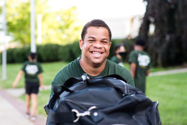 A Laker Move-In Crew member pushing one of the gray move-in bins while facing the camera and smiling