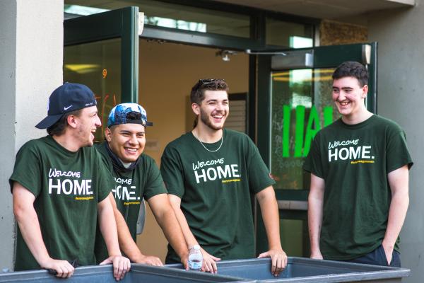 Four Laker Move-In Crew Members standing behind a couple gray move-in bins and laughing