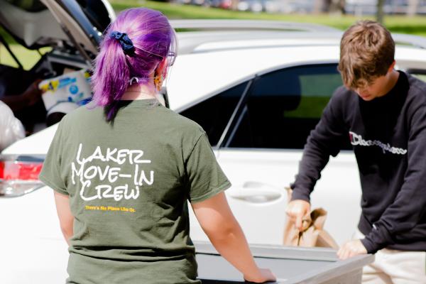 A Laker Move-In Crew member facing away from the camera, helping a student with putting their items in a gray move-in bin