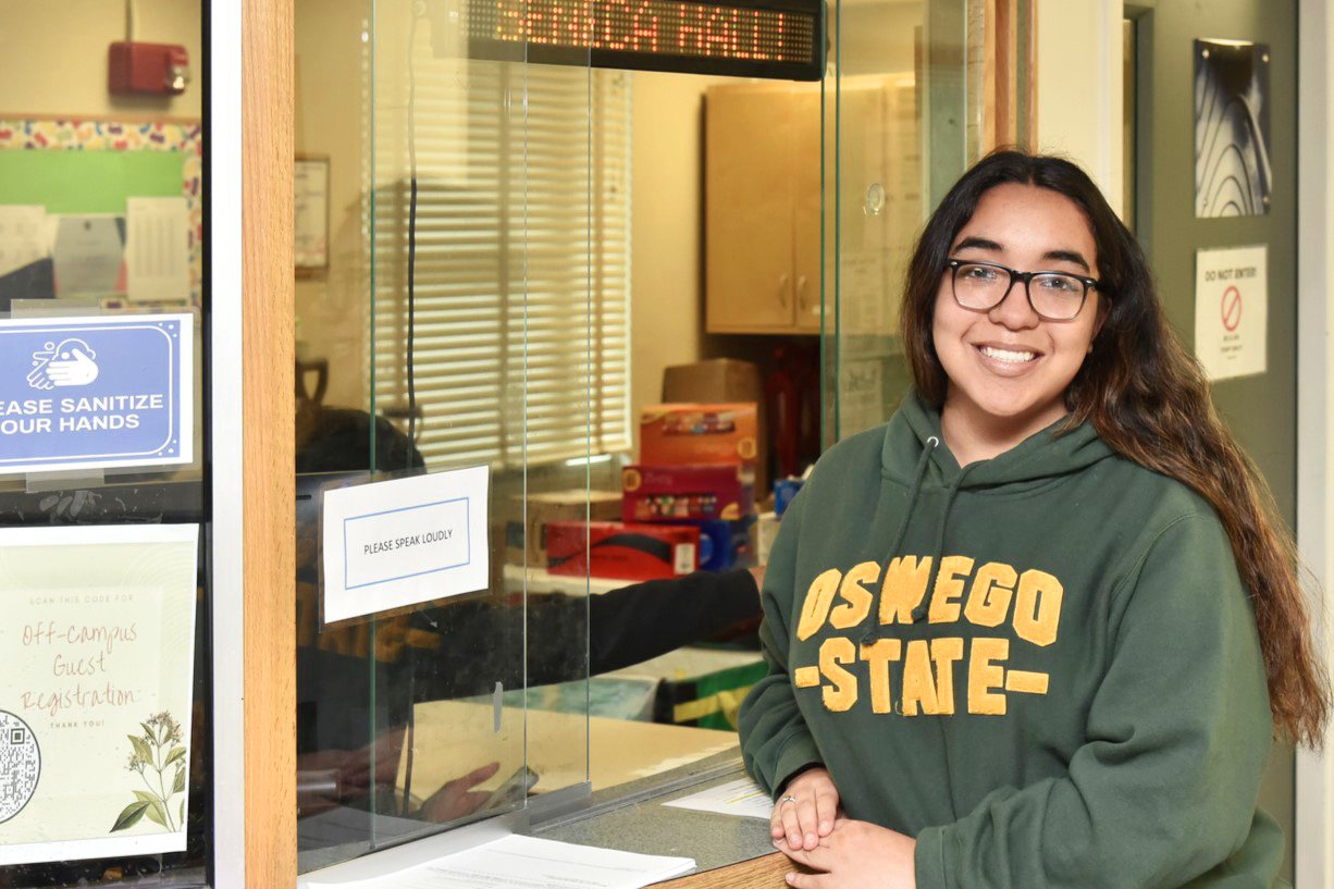 A student standing to the right of the front desk located on the first floor of Seneca Hall