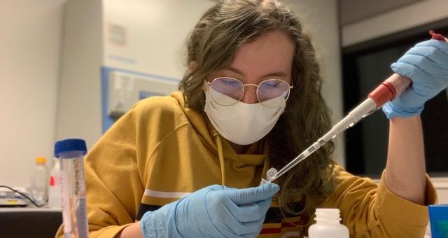 Woman pipetting into a snap-cap tube, wearing gloves and a mask