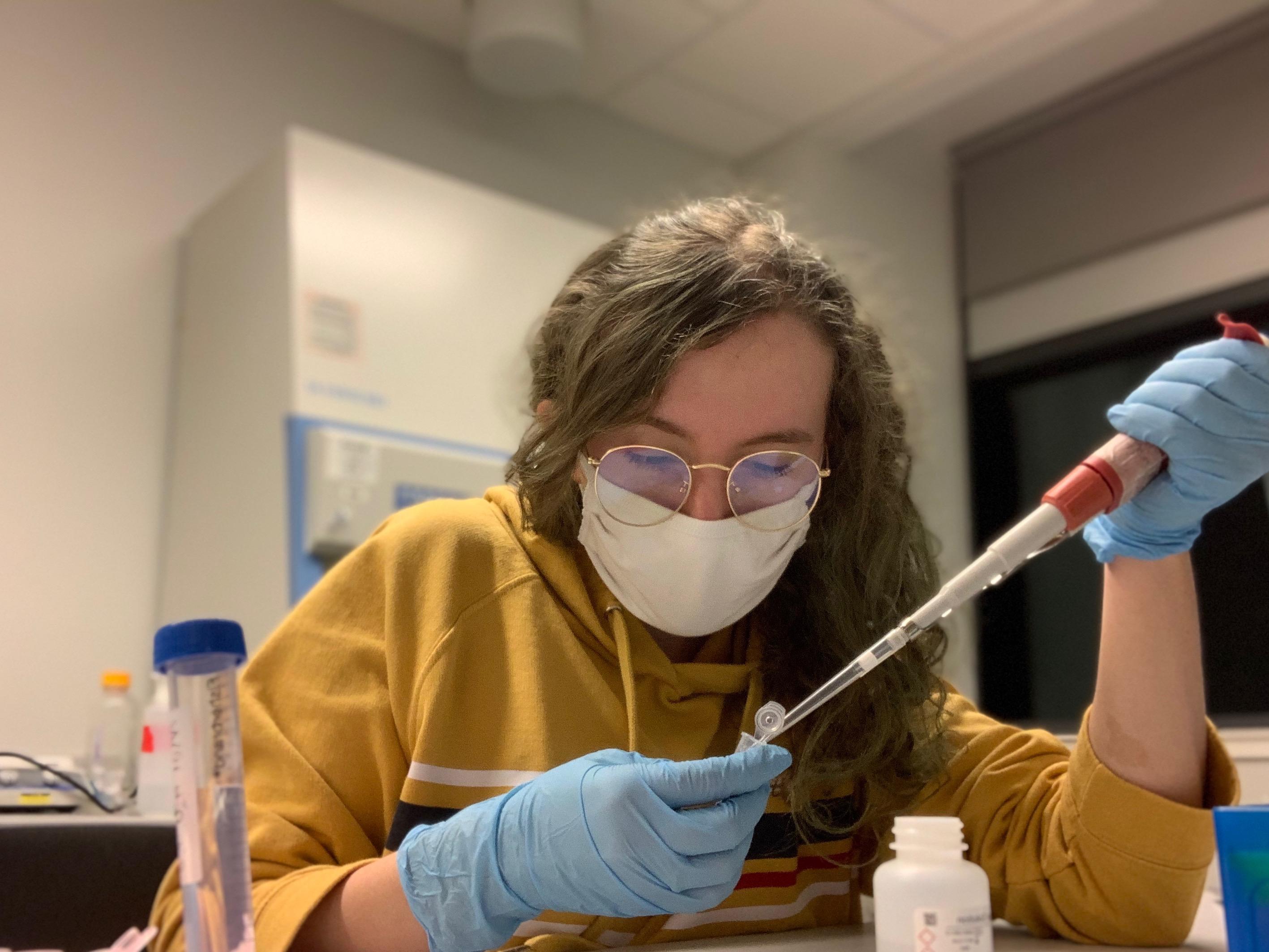 Woman pipetting into a snap-cap tube, wearing gloves and a mask