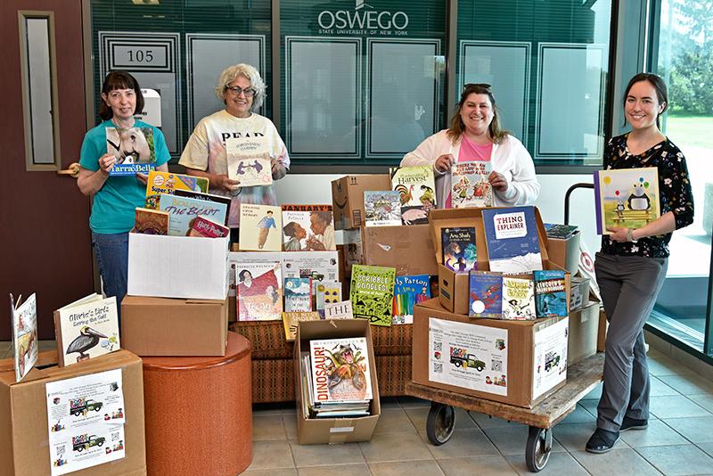 four people stand near a large stack of children's books in boxes