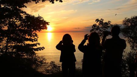 3 silhouettes of people taking photos of the Oswego sunset